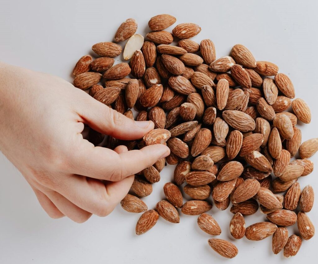 Crop person taking almond nut from white table
